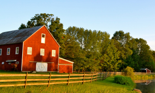 A fenced in red barn at sunset.